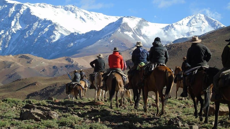 Riders on a trans-Andes trek with gauchos, snow-capped peaks behind.